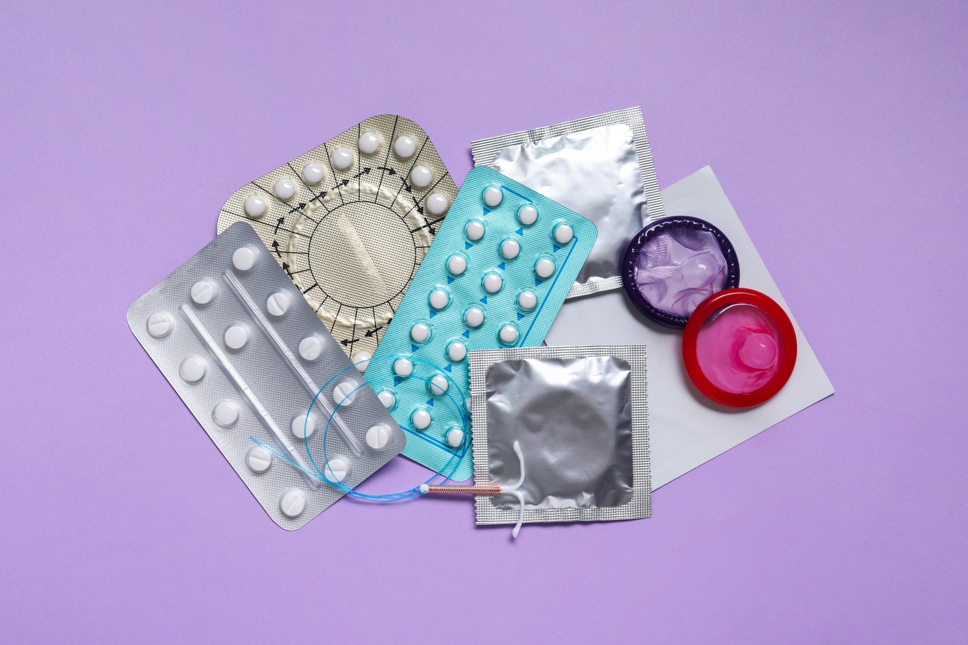 Contraceptive pills, condoms and intrauterine device on violet background, flat lay. Different birth control methods